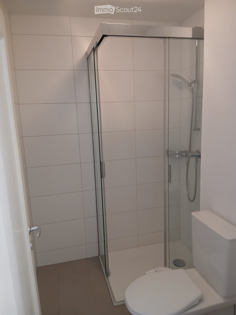Modern bathroom with white tiled walls, a glass-enclosed shower, and a toilet.