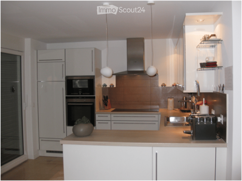 Modern kitchen with white cabinets, stainless steel appliances, pendant lights, and a central island with a plant on the counter.