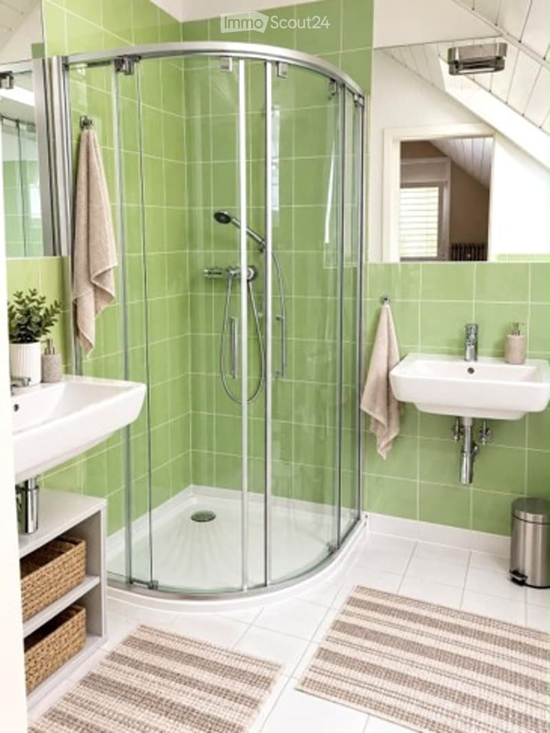 Modern bathroom with green tiled walls, a glass-enclosed shower, two sinks, and decorative towels.