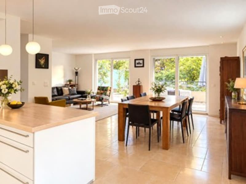 Bright, open-plan living and dining area with modern furniture, large windows, and a kitchen island.