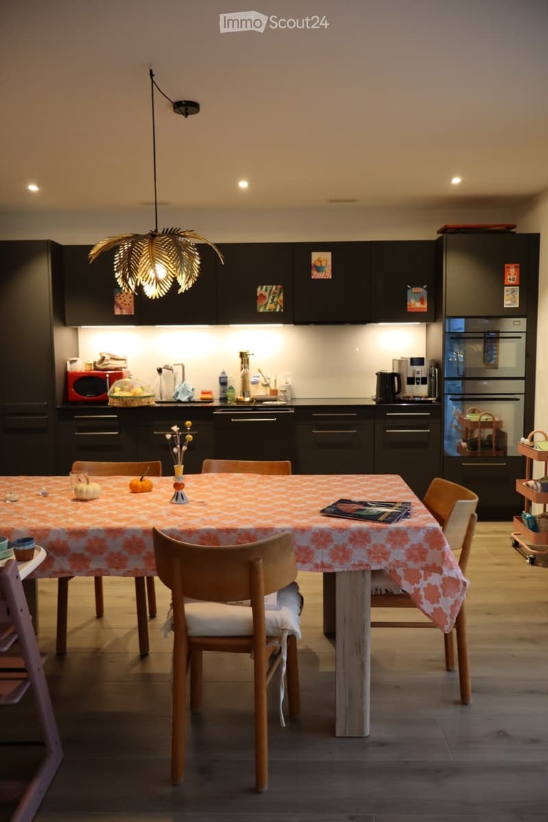 Modern kitchen with dark cabinets, a dining table with chairs, and various appliances including a microwave, refrigerator, and oven. The table is set with a patterned tablecloth, pumpkins, and decorative items.