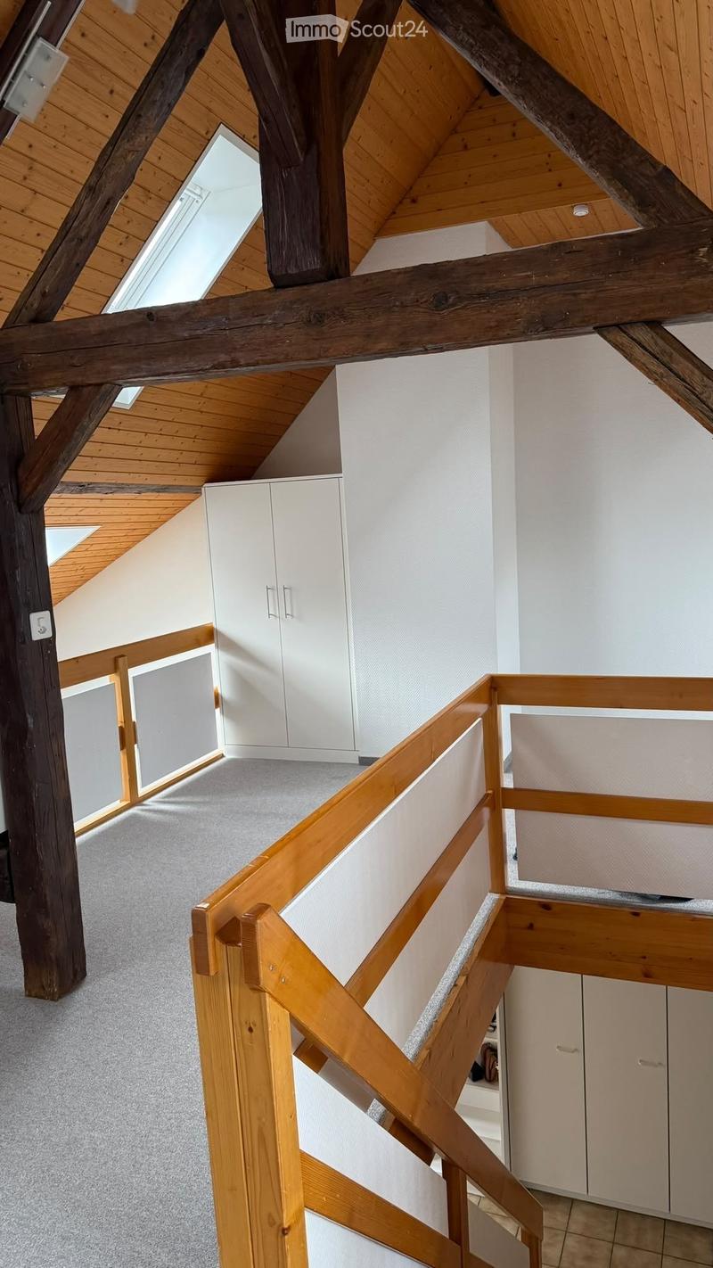 Wooden staircase with white cabinets and exposed wooden beams, leading to a room with a skylight window.