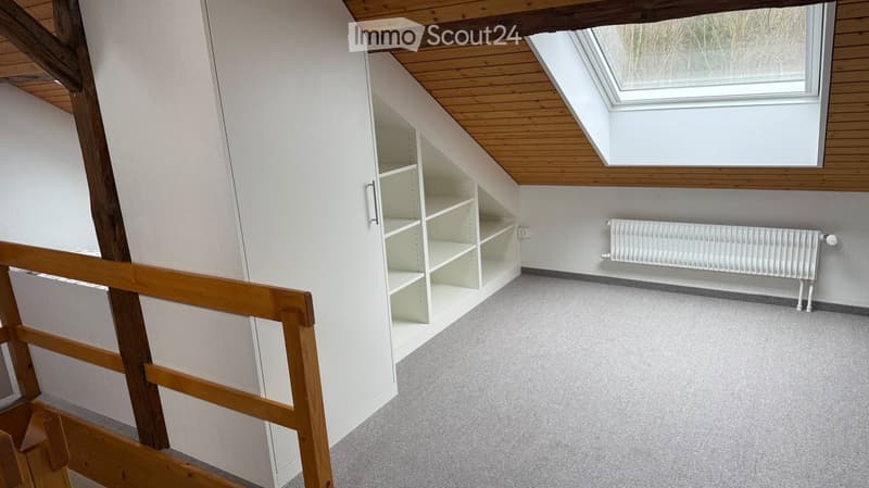 Empty room with wooden beams, built-in shelving, radiator, and skylight window.