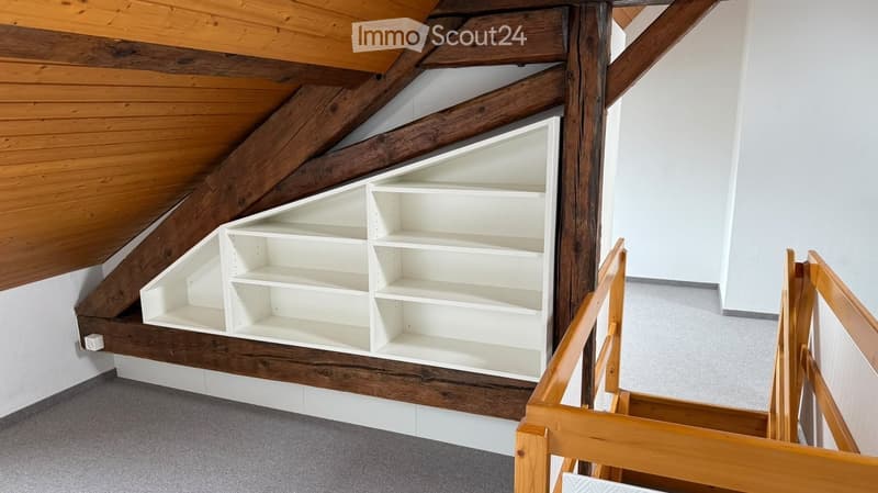 Staircase with wooden railings and built-in white shelving unit against a slanted wooden ceiling.