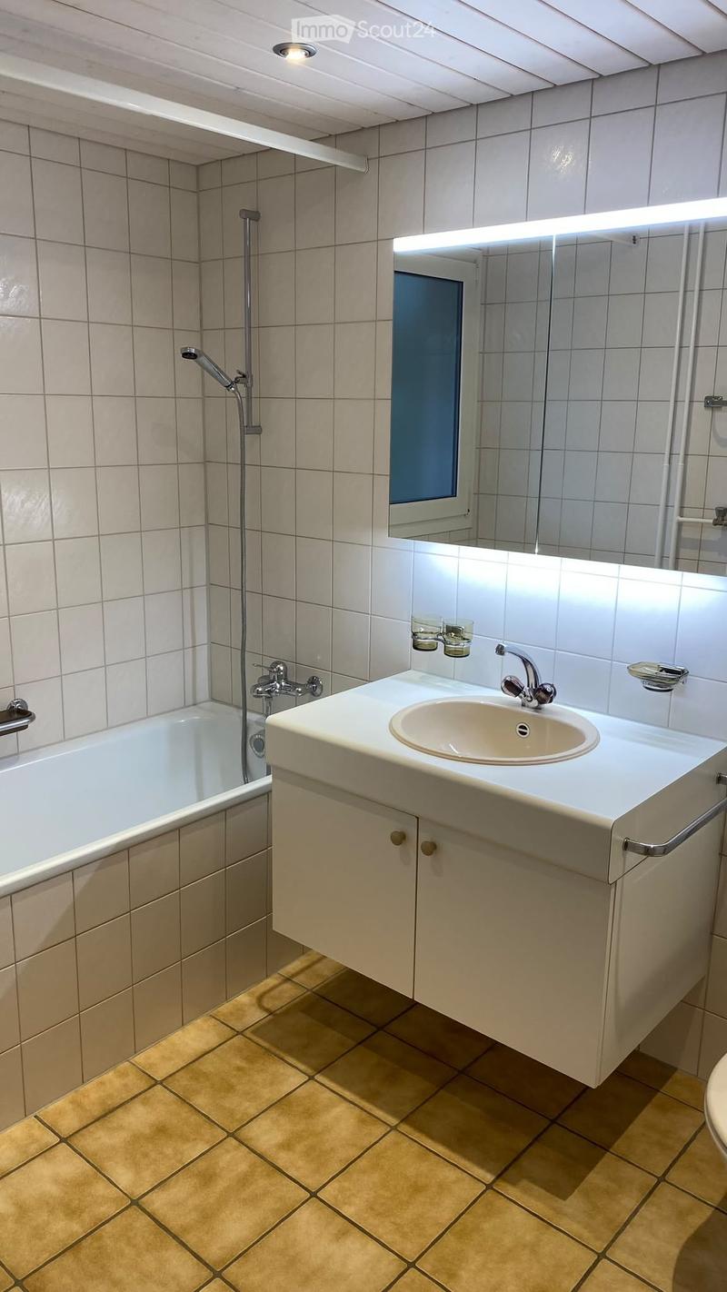 Bathroom with a bathtub, sink, and mirror. The sink has a modern faucet and is mounted on a white cabinet. The walls are tiled in beige, and the floor is covered with yellow tiles.