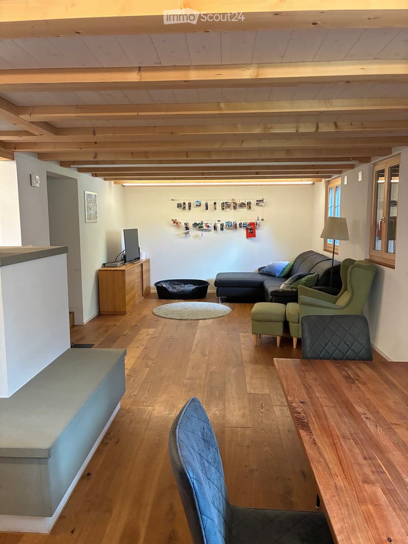 Living room with wooden floor, exposed wooden ceiling beams, sofa, armchair, coffee table, lamp, TV, dog bed, and picture frame on wall.