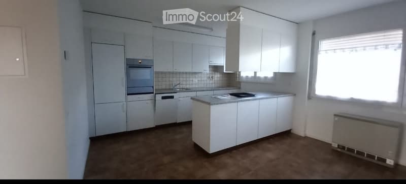 Modern kitchen with white cabinets, stainless steel appliances, and a central island. The space features a tiled backsplash and a window with blinds.