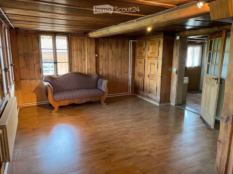Wooden-paneled room with hardwood floor, exposed wooden ceiling beams, and a single sofa against the wall.