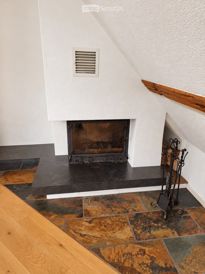 Modern fireplace with black marble surround and wooden flooring, featuring a decorative fireplace tool set nearby.
