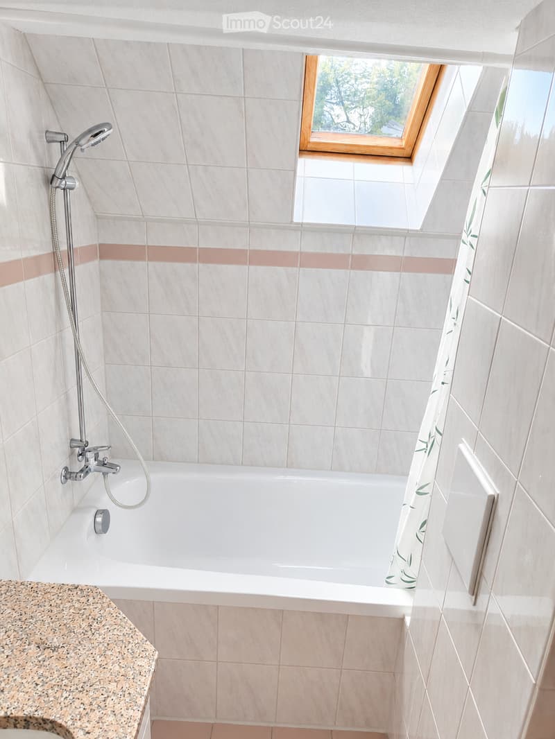 Bathroom with a white bathtub, tiled walls, a showerhead, and a window with wooden frame.