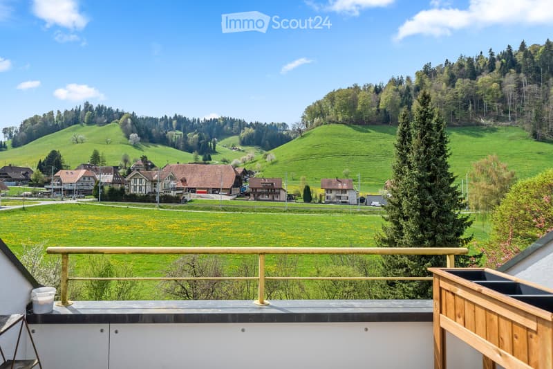 Balcony overlooking a scenic countryside with green hills, scattered houses, and trees.