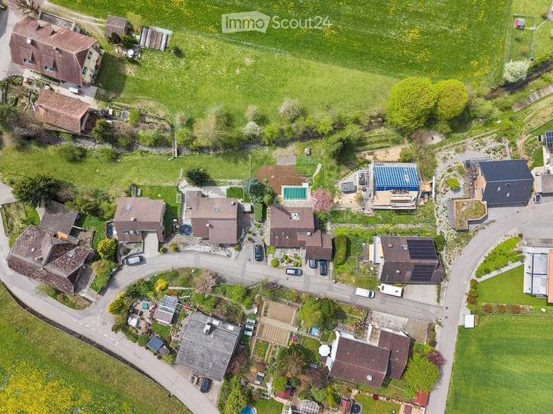 Aerial view of a residential neighborhood with multiple houses, gardens, driveways, and parked cars.