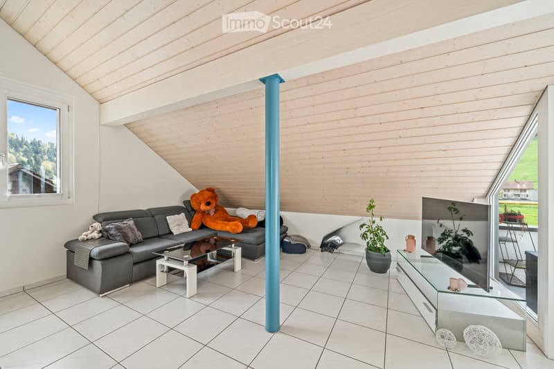Modern living room with a grey sectional sofa, coffee table, large window, and decorative items including a large teddy bear and plants.