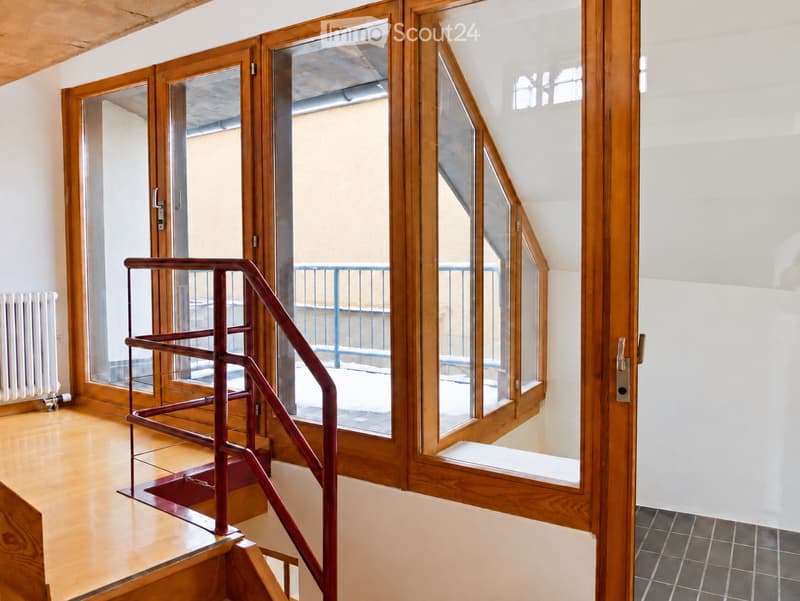 Bright hallway with wooden floors, large glass doors leading to a balcony, and a red metal staircase railing.