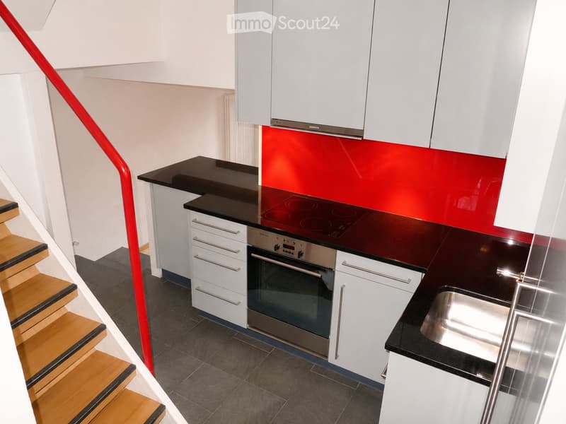 Modern kitchen with white cabinets, black countertops, stainless steel appliances, and a red accent wall.