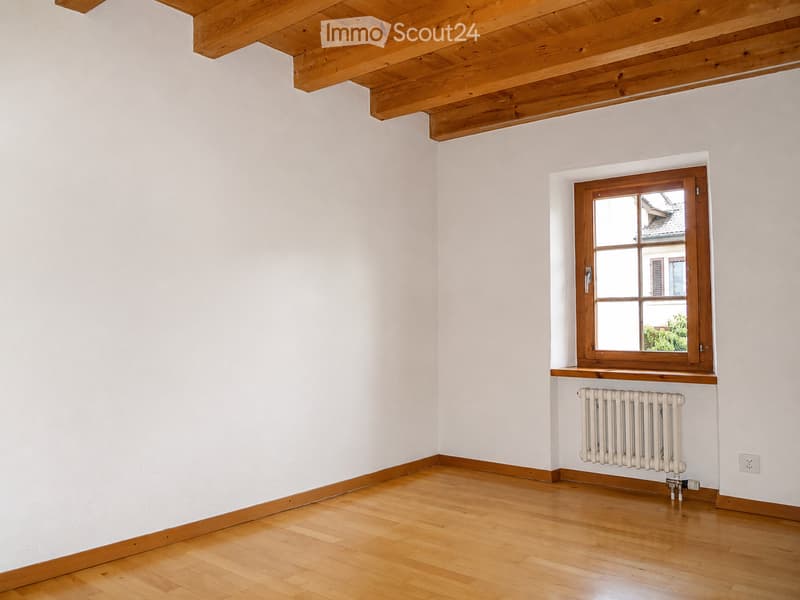 Empty room with light-colored wooden flooring, white walls, and a wooden window with a radiator below it.