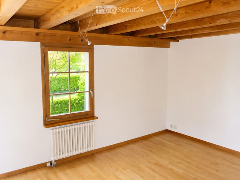 Empty room with wooden flooring, white walls, a large window with wooden frame, and a radiator below the window.