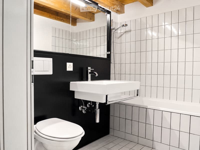 Modern bathroom with white tiles, black accent wall, white sink, toilet, bathtub, and shower area with glass enclosure.
