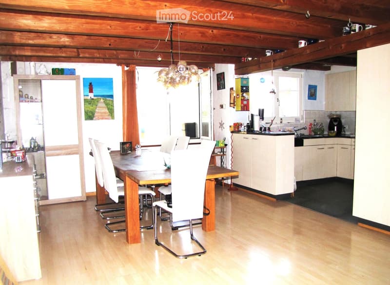 Open-plan living and dining area with wooden floors, a dining table with chairs, a kitchen area with cabinets, sink, and appliances, and a chandelier hanging from the ceiling.