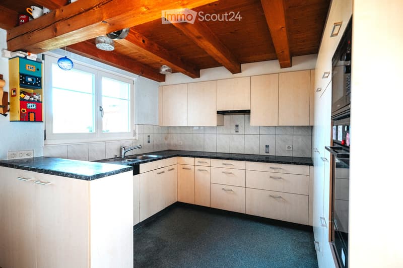 Bright kitchen with light-colored cabinets, a black countertop, and a sink. The room features a wooden ceiling with exposed beams and large windows allowing natural light to fill the space.