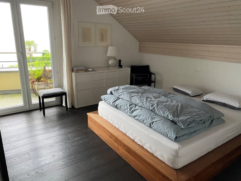 Cozy bedroom with a wooden bed, nightstand, lamp, and a view to a balcony. Includes a chair, stool, and cabinet.