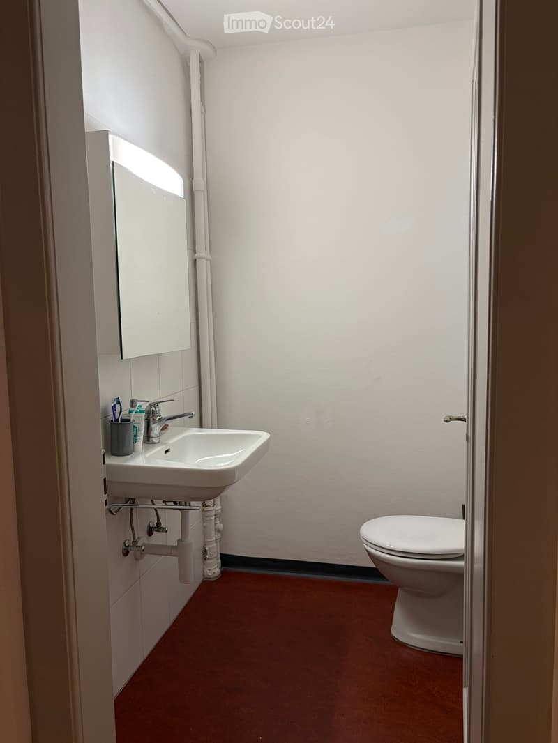 Small bathroom with a white sink, faucet, toilet, mirror, and a cup on the sink counter.