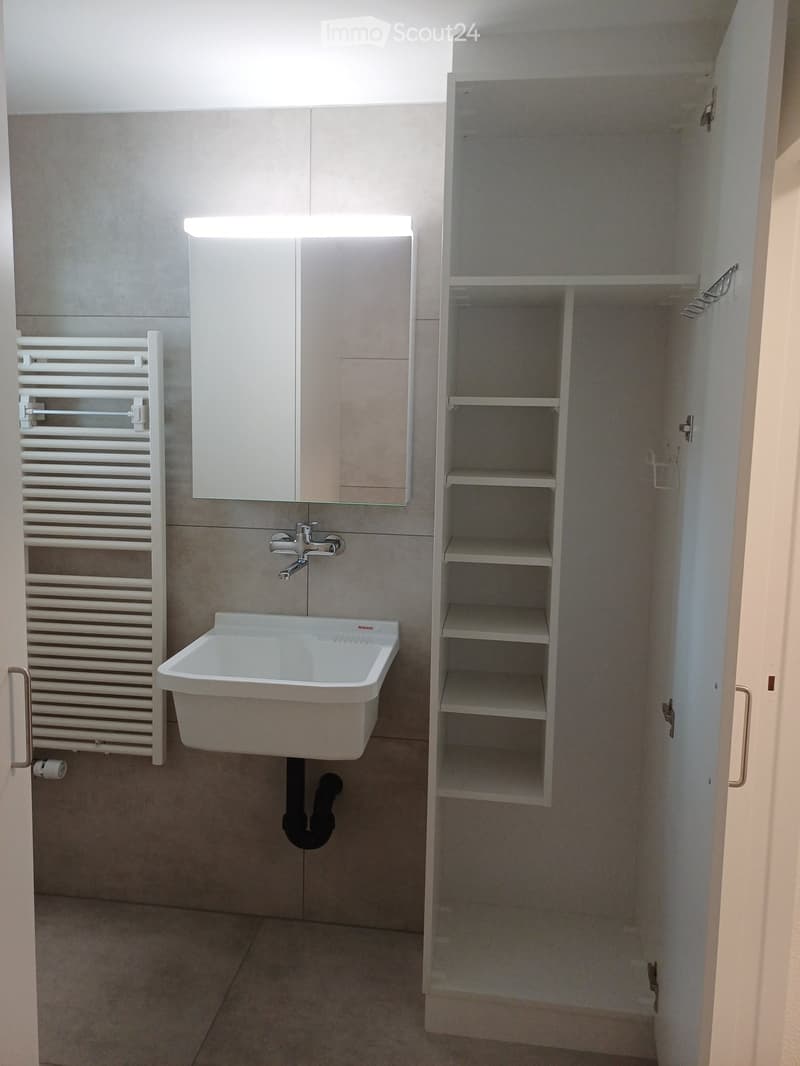 Modern bathroom with a white sink, faucet, mirror cabinet, radiator, and open shelving unit.