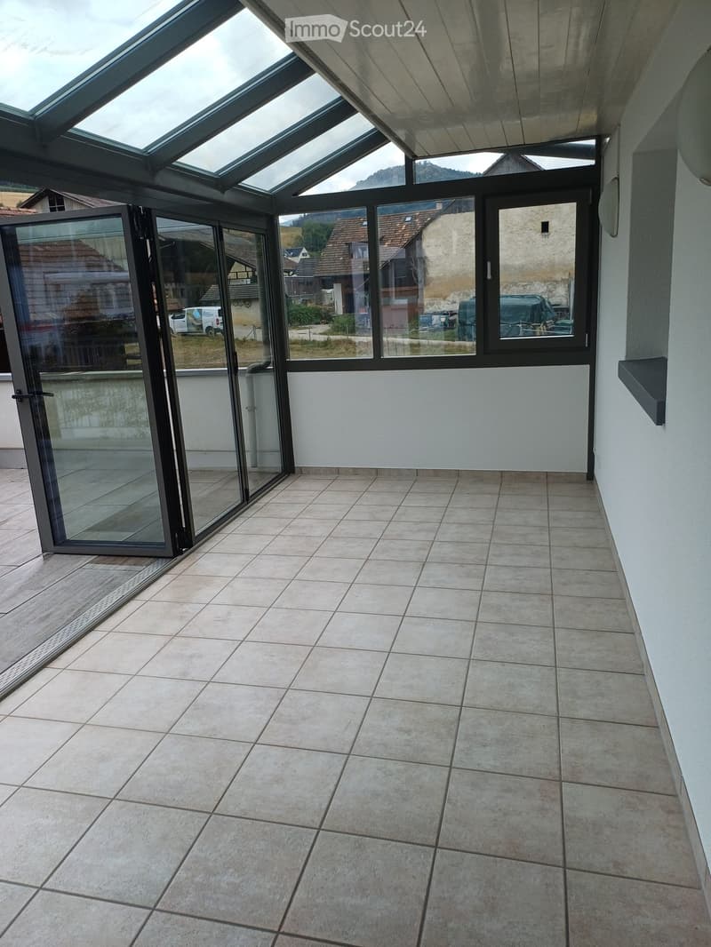 Spacious balcony with large glass doors, tiled floor, and a view of the surrounding area.