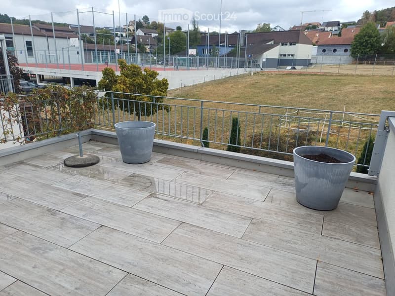 Balcony with wooden decking, metal railing, and two large grey planters.