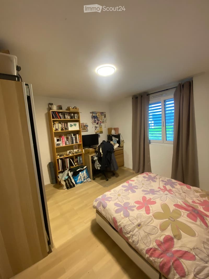 Bedroom with a bed, bookshelf, desk, chair, laptop, and window with curtains.