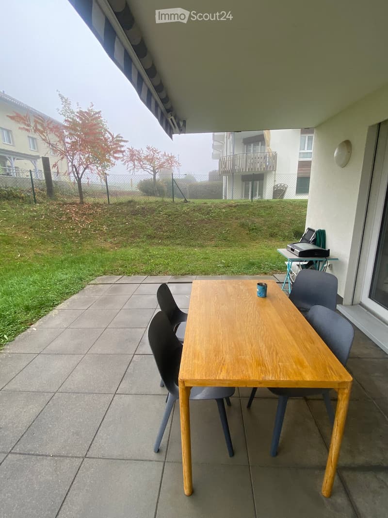 Balcony with a wooden table, four chairs, and a small side table with a printer and other items.