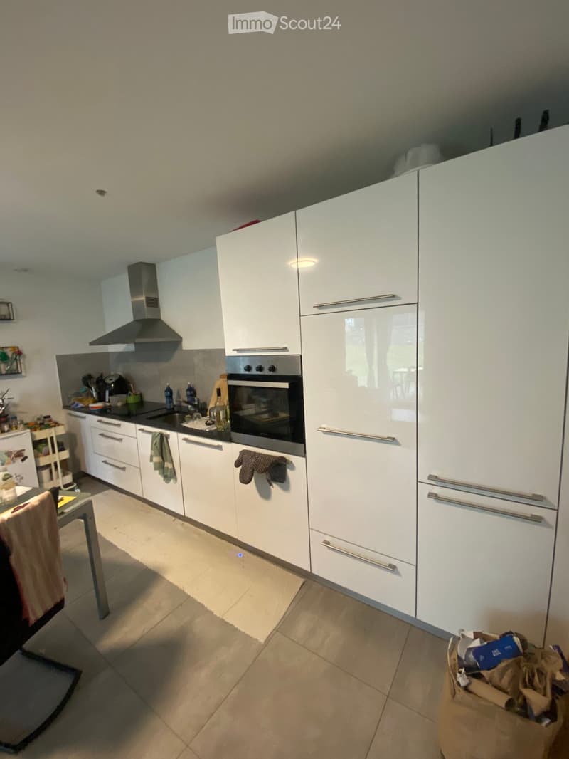 Modern kitchen with white cabinets, stainless steel oven, sink, and countertop. Includes a small dining area with a table and chair.