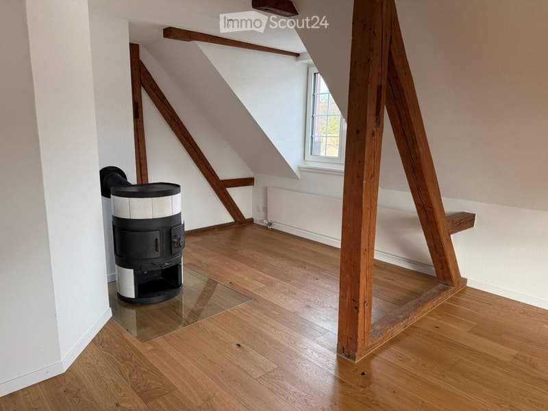 wooden flooring, exposed wooden beams, black wood-burning stove on a glass table, white walls, small window