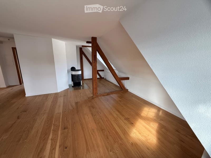 empty attic room with wooden flooring and white walls, wooden beam support and small waste bin in center