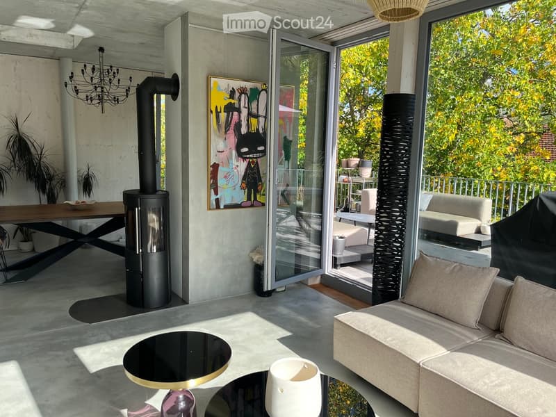 Modern living room with a fireplace, sofa, coffee table, dining area, and large windows overlooking a garden.