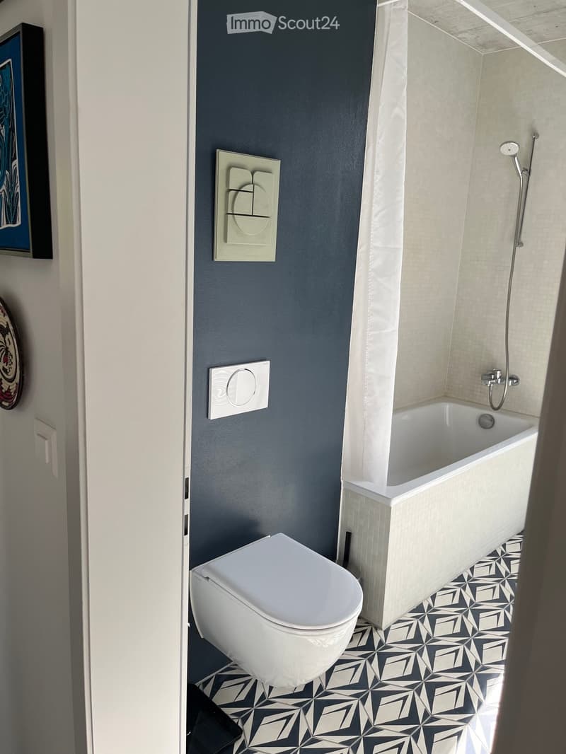Modern bathroom with dark blue walls, white toilet, bathtub, and geometric black and white tiled floor.