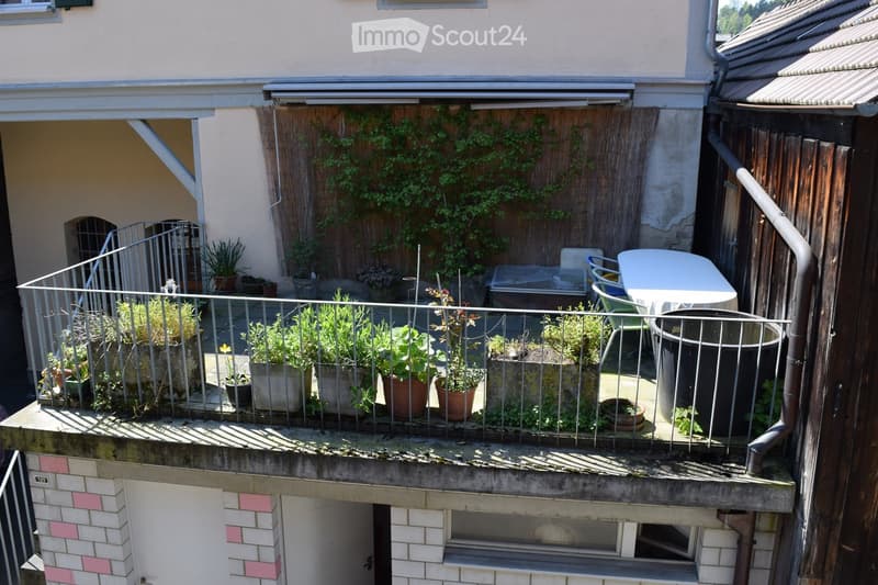 Balcony with metal railing, several potted plants, a small table, and chairs.