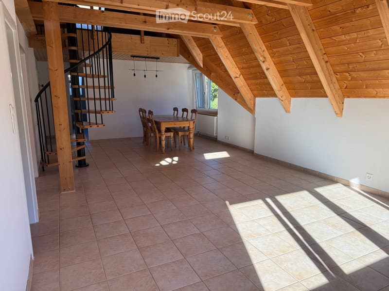 Bright dining area with wooden dining table and chairs, exposed wooden beams, and a spiral staircase leading to an upper level.