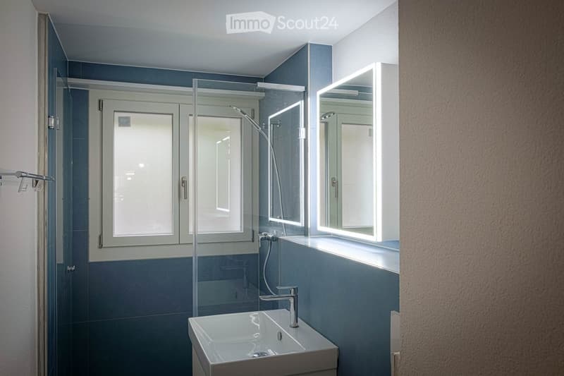 Modern bathroom with a white sink, chrome faucet, illuminated mirrors, and a glass-enclosed shower area.