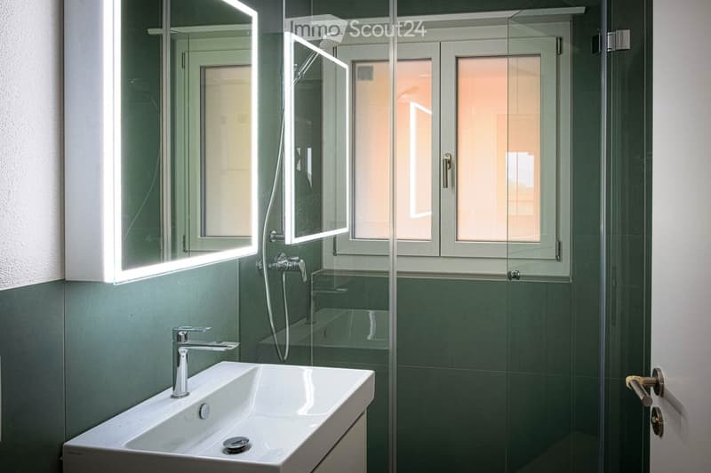 Modern bathroom with a white sink, chrome faucet, illuminated mirror, glass shower enclosure, and a showerhead.