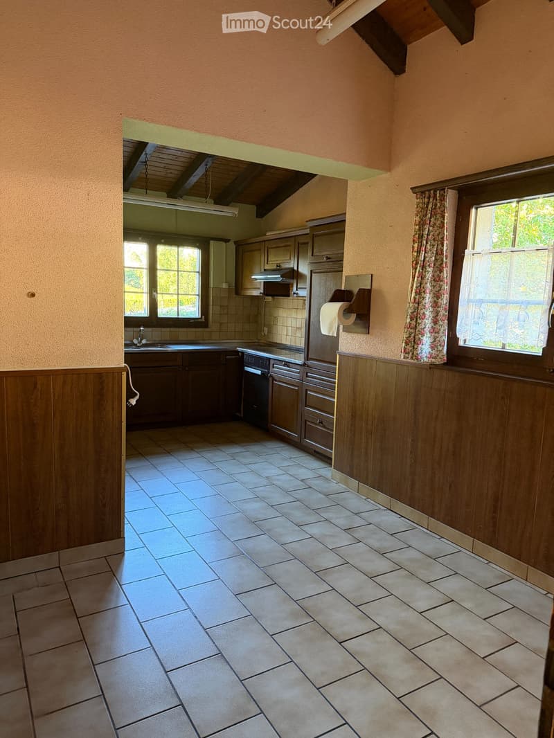 Empty kitchen with tiled floor, wooden cabinets, sink, and windows with floral curtains.