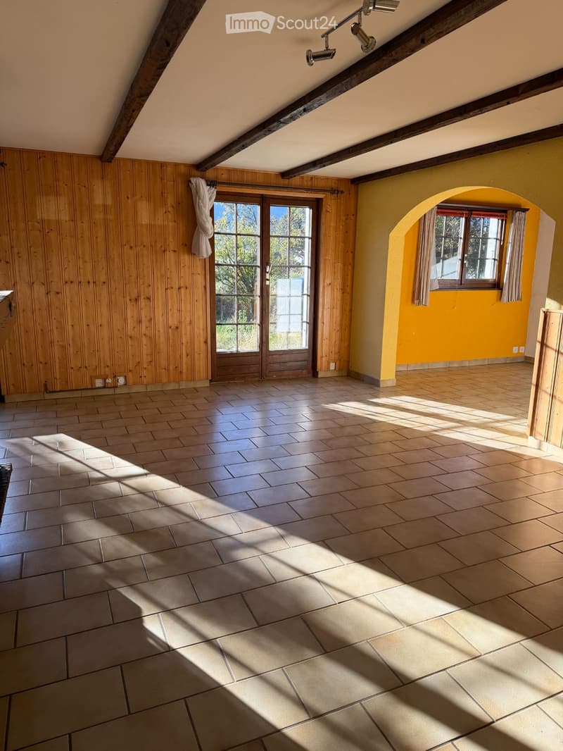 Empty room with wooden walls, tiled floor, large windows, and exposed wooden beams on the ceiling.