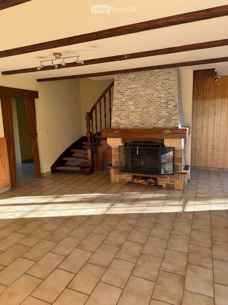 Hallway with tiled floor, wooden staircase, and a brick fireplace with a glass enclosure and wood logs inside.