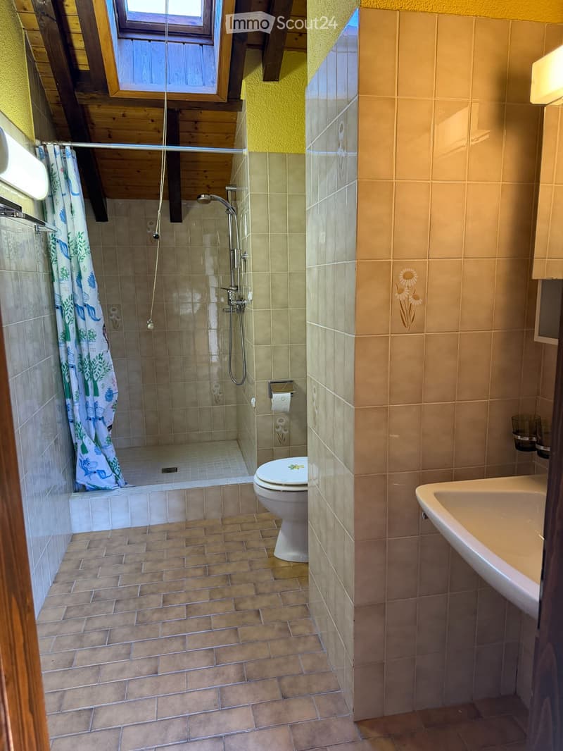 Bathroom with tiled walls and floor, featuring a toilet, sink, and a walk-in shower with a curtain.