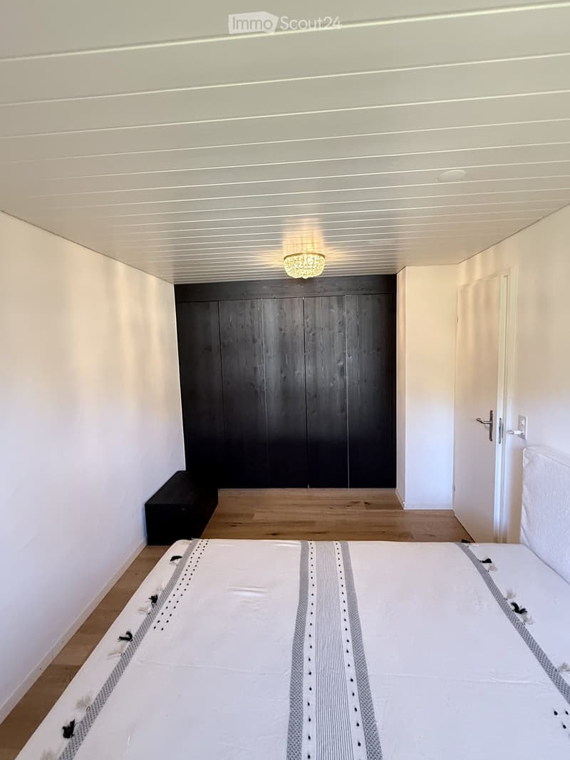 Modern bedroom with a large bed, a dark wooden wardrobe, and a small bench near the wall.