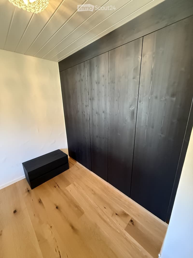 Empty hallway with light wooden flooring, white walls, and dark wooden built-in closet units.