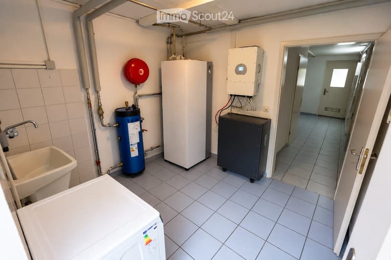 Utility bathroom with tiled walls and floor, featuring a water heater, storage unit, emergency valve, and a small sink area with a faucet.