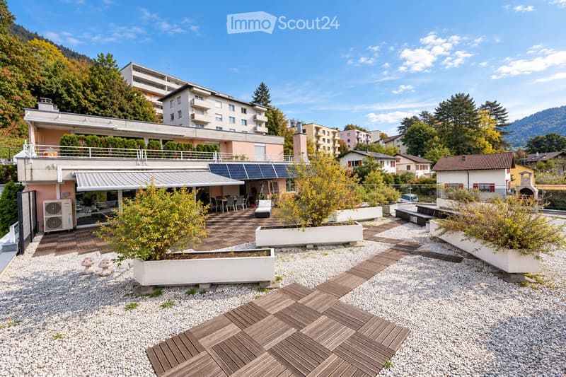Rooftop terrace with wooden decking, potted plants, seating area, and solar panels on the adjacent building.