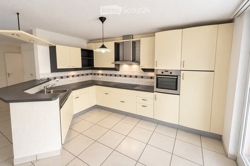 Modern kitchen with light-colored cabinets, black countertops, a sink, an oven, and a range hood. The space features tiled flooring and walls with a decorative backsplash.