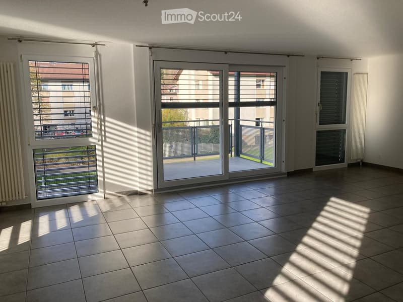 Empty room with tiled floor, large sliding glass doors leading to a balcony, and windows with blinds.